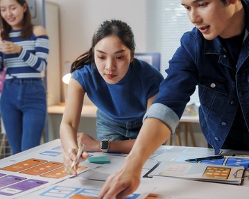 Three people are working at a table with prototypes and notes as they brainstorm ideas for a project.