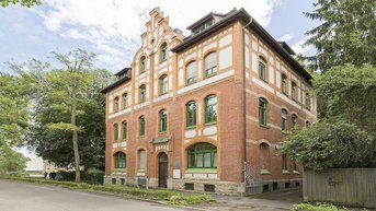 Historic building with a red brick facade, large windows, and decorative elements, surrounded by trees and green spaces.
