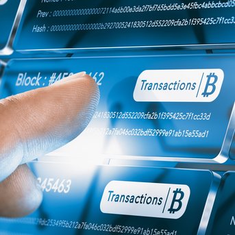 A hand points to digital transaction data with block numbers and hash values on a screen.