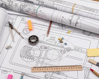 Technische Zeichnungen und Pläne liegen ausgebreitet auf einem Tisch, umgeben von Zeichenwerkzeugen, einem Zirkel, Schrauben und einem Lineal.