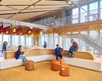 Modern interior design featuring a wooden bench, seating areas, and several people interacting in a bright, open space.