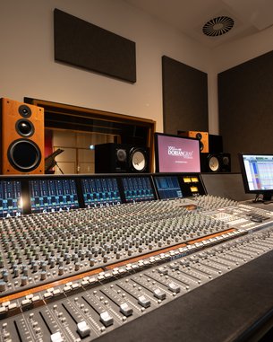 Tonstudio mit Mischpult, Lautsprechern und Computerbildschirm. Akustikpaneele an den Wänden zur Schallisolierung.
