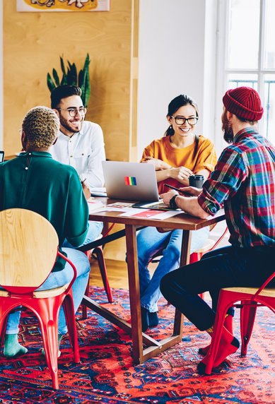Fünf Personen sitzen an einem Tisch, arbeiten an Laptops und diskutieren. Der Raum ist hell und modern eingerichtet.