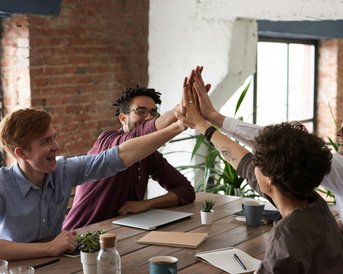 Vier Personen in einem Besprechungsraum geben sich gegenseitig High-Fives, um Teamgeist und Zusammenarbeit zu feiern.
