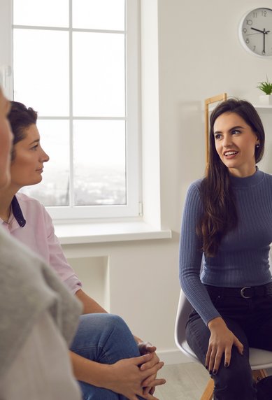 Eine Gruppe von Frauen sitzt in einem hellen Raum. Eine Frau in blauer Kleidung spricht, während die anderen aufmerksam zuhören.