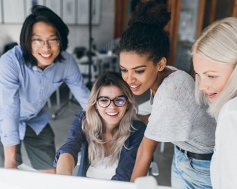 Vier Personen stehen um einen Computer und schauen auf den Bildschirm. Sie scheinen an einem Projekt oder einer Präsentation zu arbeiten.