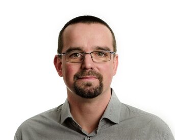 A man with glasses and short hair is wearing a checked shirt. He is looking directly at the camera.