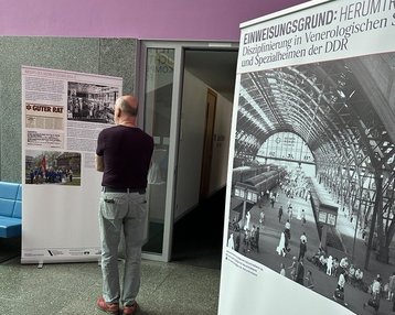 Ein Besucher betrachtet zwei Ausstellungstafeln, die Informationen über die Disziplinierung in der DDR und historische Fotografien zeigen. Eine Tafel enthält den Titel "GUTER RAT". Der Raum hat eine moderne Architektur.