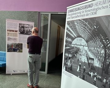Ein Besucher betrachtet zwei Ausstellungstafeln, die Informationen über die Disziplinierung in der DDR und historische Fotografien zeigen. Eine Tafel enthält den Titel "GUTER RAT". Der Raum hat eine moderne Architektur.