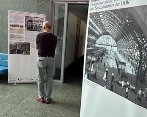 A visitor examines two exhibition panels that display information about discipline in the GDR and historical photographs. One panel is titled "GOOD ADVICE." The room features modern architecture.