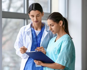 Zwei medizinische Fachkräfte besprechen Informationen auf einem Clipboard, während sie in einem hellen Raum stehen.