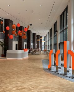Moderne Empfangshalle mit Holzfußboden, großen Fenstern, einer Treppe und orangefarbenen Dekorationen.