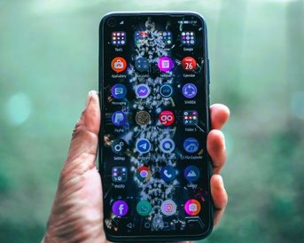 A smartphone is held in one hand, displaying various app icons on the screen with a blurred background.