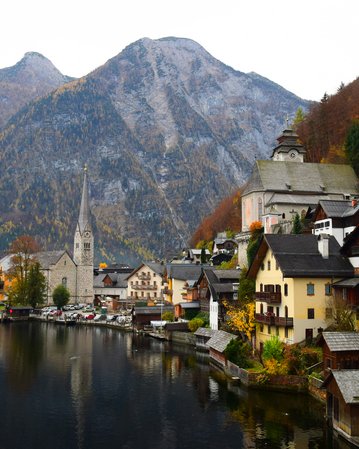 Blick auf das malerische Dorf Hallstatt am See, umgeben von Bergen und herbstlichen Bäumen. Historische Gebäude und eine Kirche sind sichtbar.