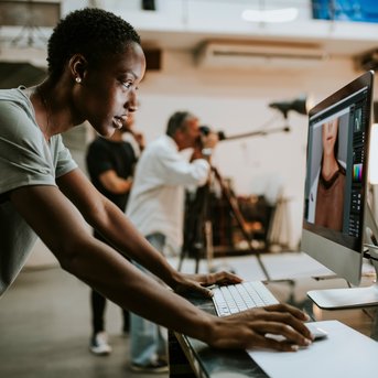 A person is working on a computer in a photo studio, while other photographers are taking pictures in the background.