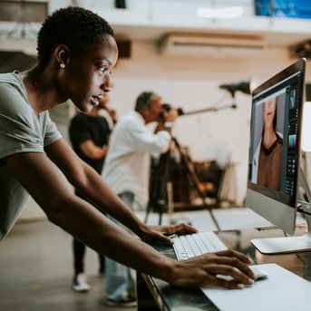 Eine Person arbeitet am Computer in einem Fotostudio, während andere Fotografen im Hintergrund Fotos aufnehmen.