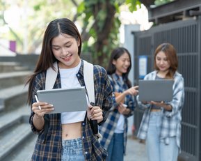 A young woman with a tablet is going down the stairs, while two other women in the background are also using tablets.