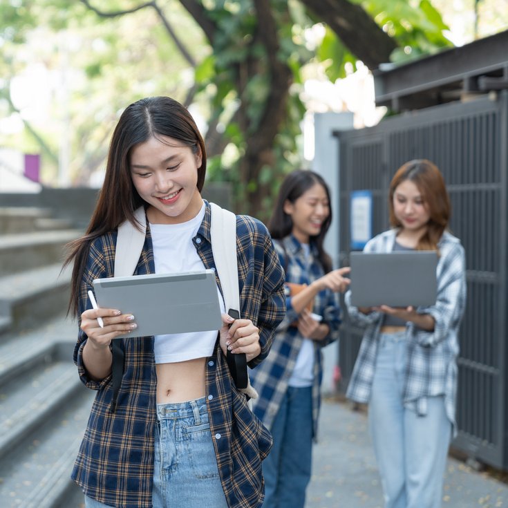A young woman with a tablet is going down the stairs, while two other women in the background are also using tablets.