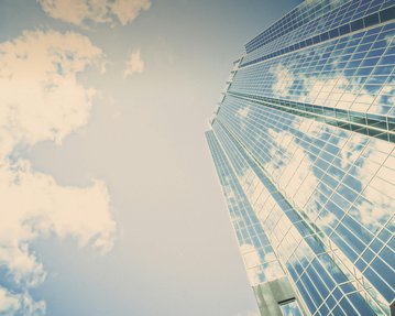 Skyscraper with reflective windows that mirror the sky and clouds. The perspective is from the bottom looking up.