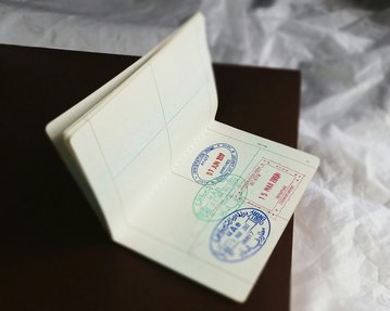 A opened passport book with several stamps, including a red stamp and two blue stamps representing various entry or exit stamps. The background is blurred and neutral.