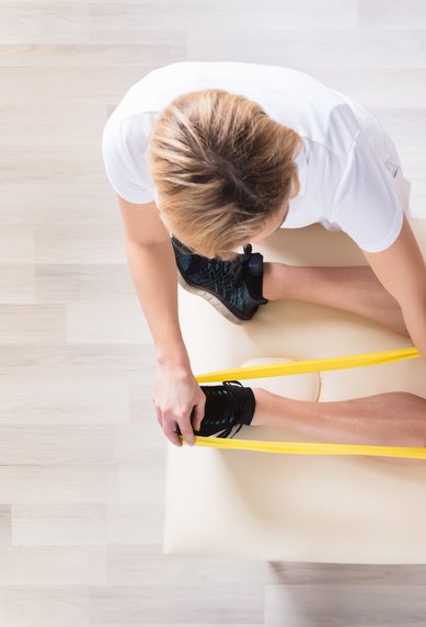 Eine Person führt mit einem Therapeuten Dehnübungen mit einem Widerstandsband durch, während sie auf einer Bank sitzt.