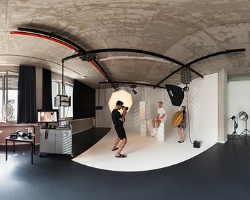 Photo studio with a photographer capturing a model on a pedestal while an assistant helps with a reflector.