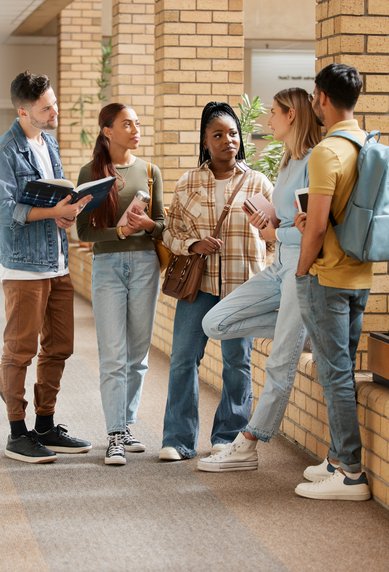 Fünf Studierende stehen in einem Flur und diskutieren. Sie halten Bücher und Notizen, während sie sich unterhalten.