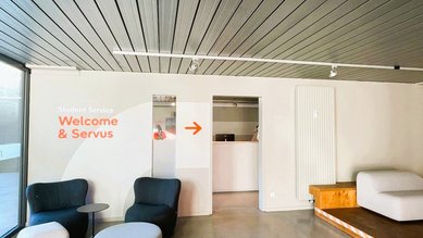 Moderne Empfangsbereich mit zwei Sitzgelegenheiten, einem Tisch und einem Hinweis auf den Studentenservice mit Richtungspfeil.