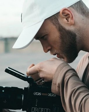 A man wearing a white cap is carefully examining a camera. He holds the camera with one hand and adjusts it with the other. The emphasis is on his concentration and the professional equipment.