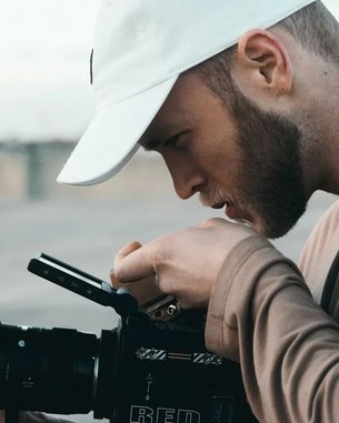 Ein Mann mit einer weißen Kappe betrachtet sorgfältig eine Kamera. Er hält die Kamera mit einer Hand und justiert sie mit der anderen. Der Fokus liegt auf seiner Konzentration und der professionellen Ausrüstung.