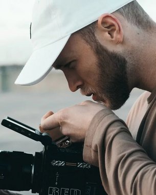 A man wearing a white cap is carefully examining a camera. He holds the camera with one hand and adjusts it with the other. The emphasis is on his concentration and the professional equipment.