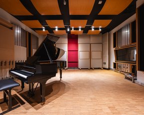 A modern recording studio featuring a black grand piano, a stool, and soundproof walls. The ceiling has an interesting design with wooden panels, and there is a warm wooden floor.