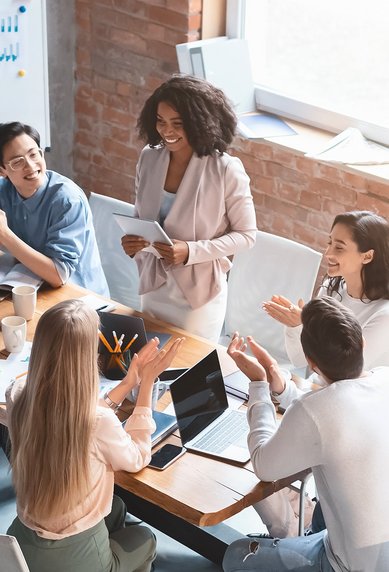 A group of nine people is sitting at a table, discussing and interacting, while one person stands and presents.