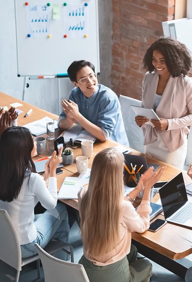 Eine Gruppe von neun Personen sitzt an einem Tisch, diskutiert und interagiert, während eine Person steht und präsentiert.