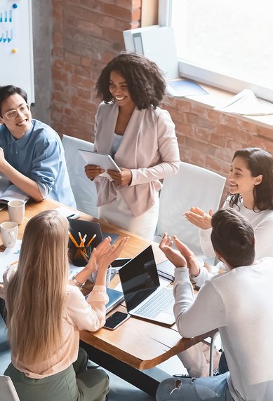 A group of nine people is sitting at a table, discussing and interacting, while one person stands and presents.