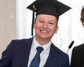 Ein graduierter Student in einem Anzug mit einer Abschlussmütze lächelt neben einem Mann in Brille und Anzug.