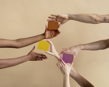 Different hands reach for colorful, geometric shapes in yellow, purple, and orange against a neutral background.