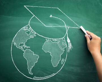 A hand is drawing a globe with a graduation cap on a green chalkboard.