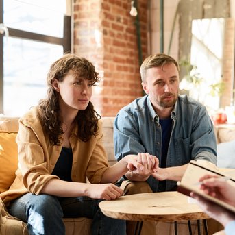 Ein Paar sitzt auf einer Couch und hält Händchen, während sie einem Berater gegenüber sitzen, der Notizen macht.