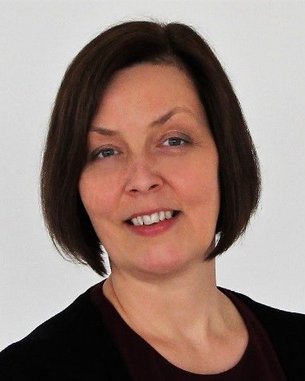 A woman with shoulder-length brown hair and a neutral expression is wearing a black top and standing against a light background.