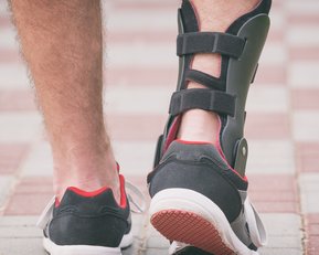 A foot in a sports shoe with a brace on it, walking along a paved path.