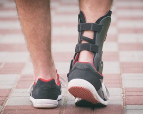 Ein Fuß mit einer Schiene, der in einem sportlichen Schuh steht, während er auf einem gepflasterten Weg geht.