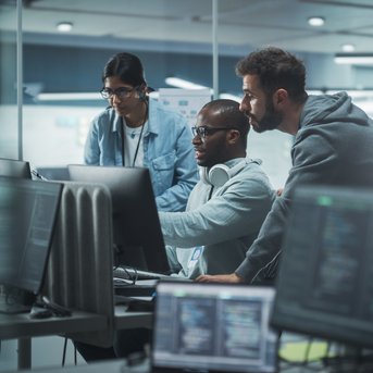 Three people are working on computers in a modern office as they collaborate on a project or solution.