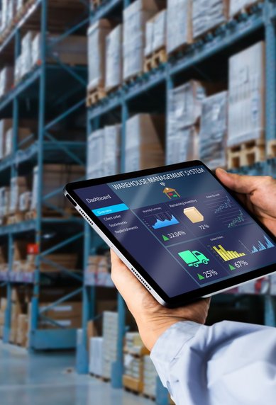 Eine Person hält ein Tablet mit Datenanalysen in einem Lagerhaus, umgeben von Regalen mit Waren.
