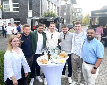 Eine Gruppe von sieben Personen steht um einen Tisch mit Getränken und Snacks, lächelnd und posierend für ein Foto.