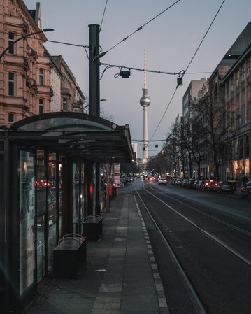 Street view with a tram stop and the Berlin TV Tower in the background, surrounded by buildings and vehicles.