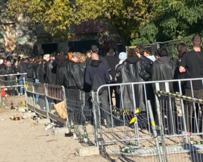 A long line of people in black clothing stands behind barriers, waiting to enter a venue.