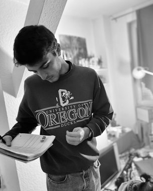 A young man is wearing a University of Oregon sweatshirt and writing in a notebook.