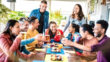 Eine Gruppe von neun Personen sitzt an einem Tisch, genießt Essen und Getränke und lacht miteinander in einer hellen, freundlichen Umgebung.