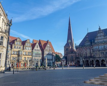 Historische Gebäude und ein Kirchturm prägen den Marktplatz, umgeben von einer klaren blauen Himmel. Die Architektur zeigt eine Mischung aus traditionellen und modernen Stilen.